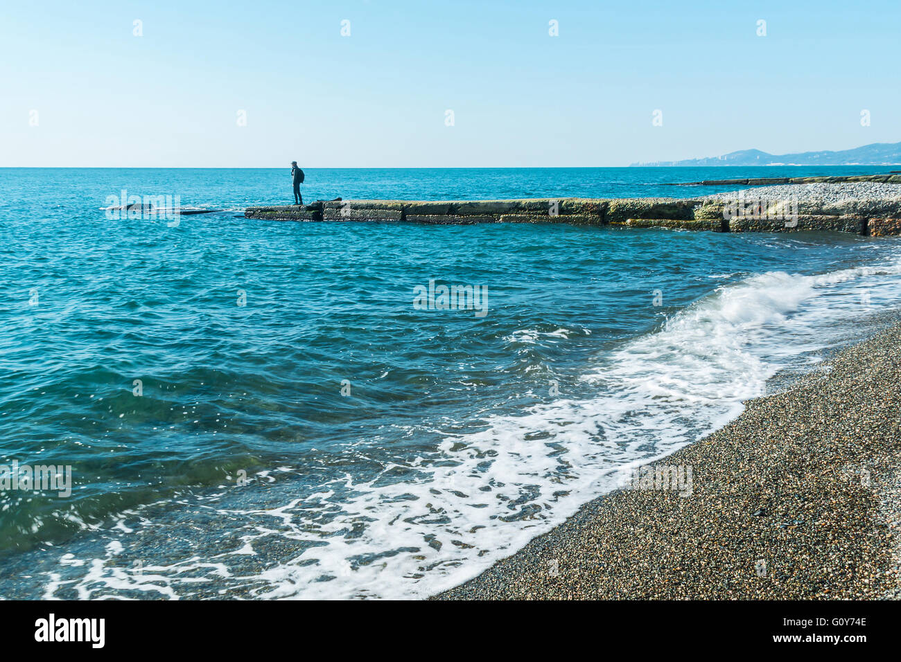 Breakwater with a silhouette of the person and pebble beach with sea views Stock Photo