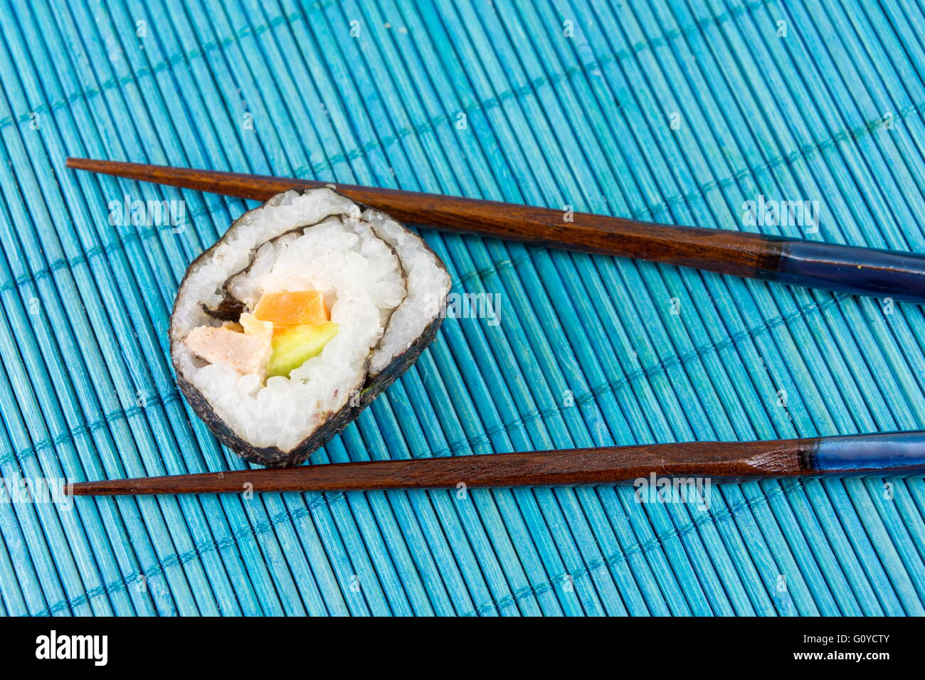 Sushi roll caught by chopsticks on blue bamboo background Stock Photo