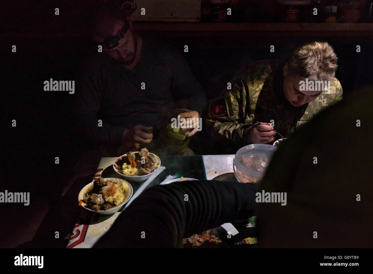 Mar 9, 2016 - Avdiivka, Ukraine - The electrical generator was knocked out during a night of shelling. The men eat a pork and plum stew by flashlight in the relative safety of their bunker. The group boasts that Right Sector has the best food on the front lines. In the now abandoned industrial outskirts of Avdiivka, Ukraine, the 74th battalion of the Ukrainian army maintains several small positions within 100 meters of those held by separatists troops of the Donetsk People's Republic (DNR). Despite the conditions of the Minsk ceasefire agreement, separatists continue to fire 82mm,120mm and 152 Stock Photo