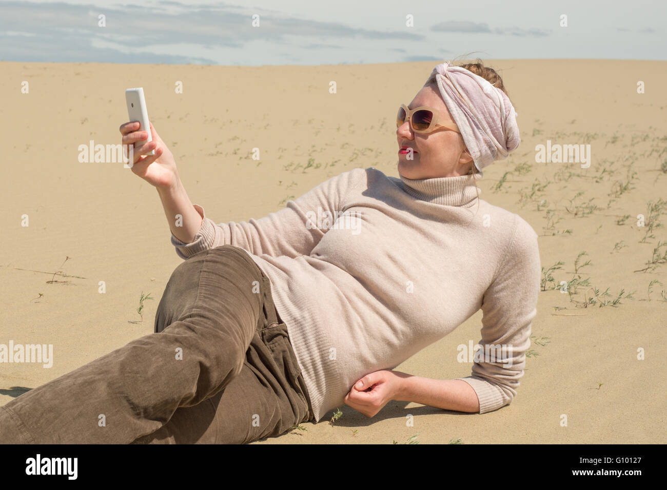 Woman lying on sand and looking at the smartphone Stock Photo