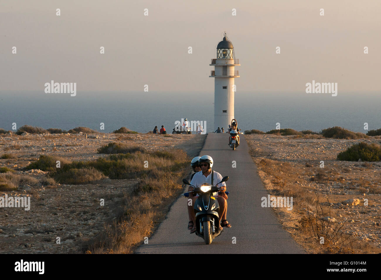 Two young motorcyclists on a long road to Es Cap de Barbaria lighthouse, in Formentera, Balears Islands. Spain. Barbaria cape formentera lighthouse road. Stock Photo