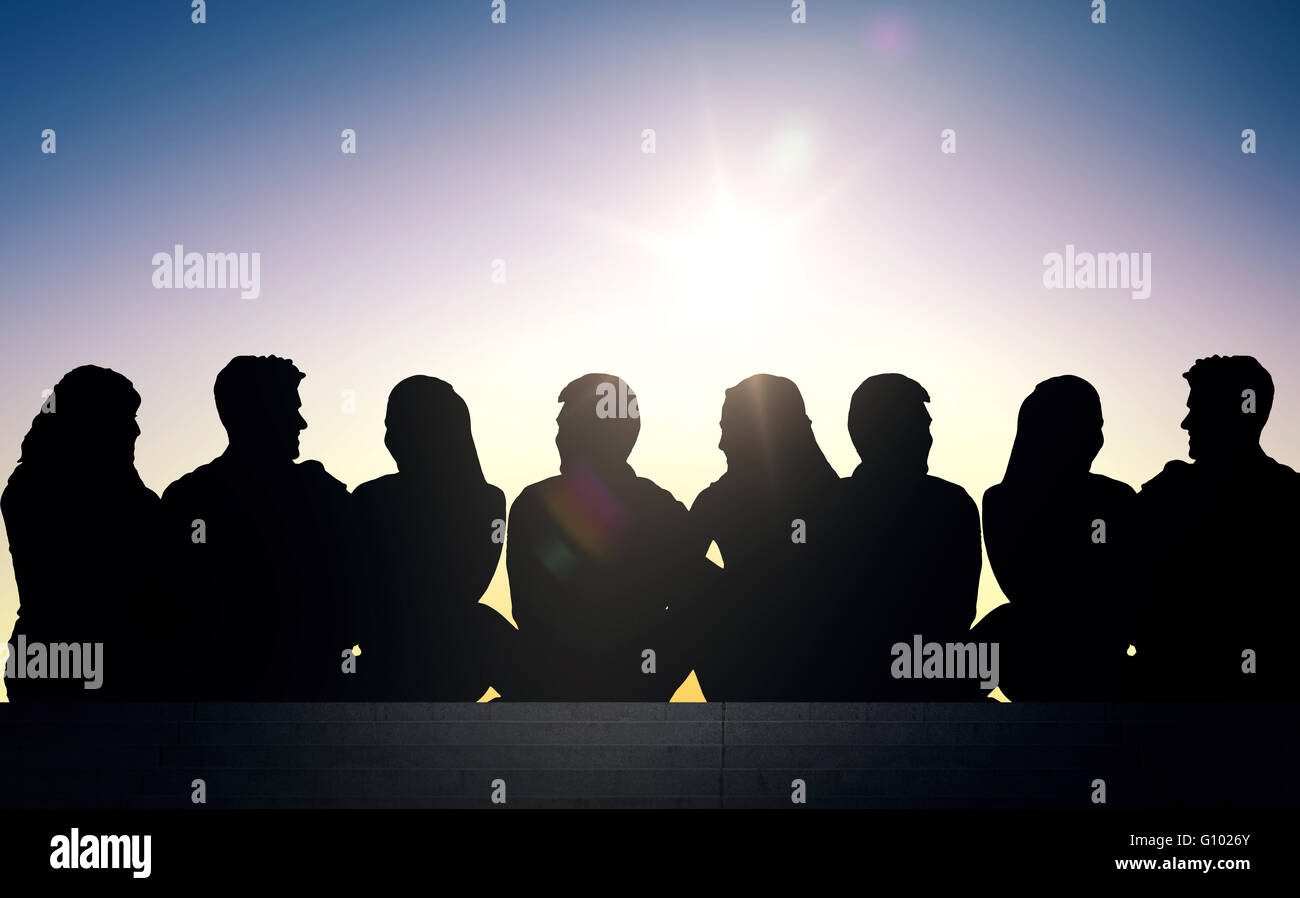 silhouettes of friends sitting on stairs over sun Stock Photo