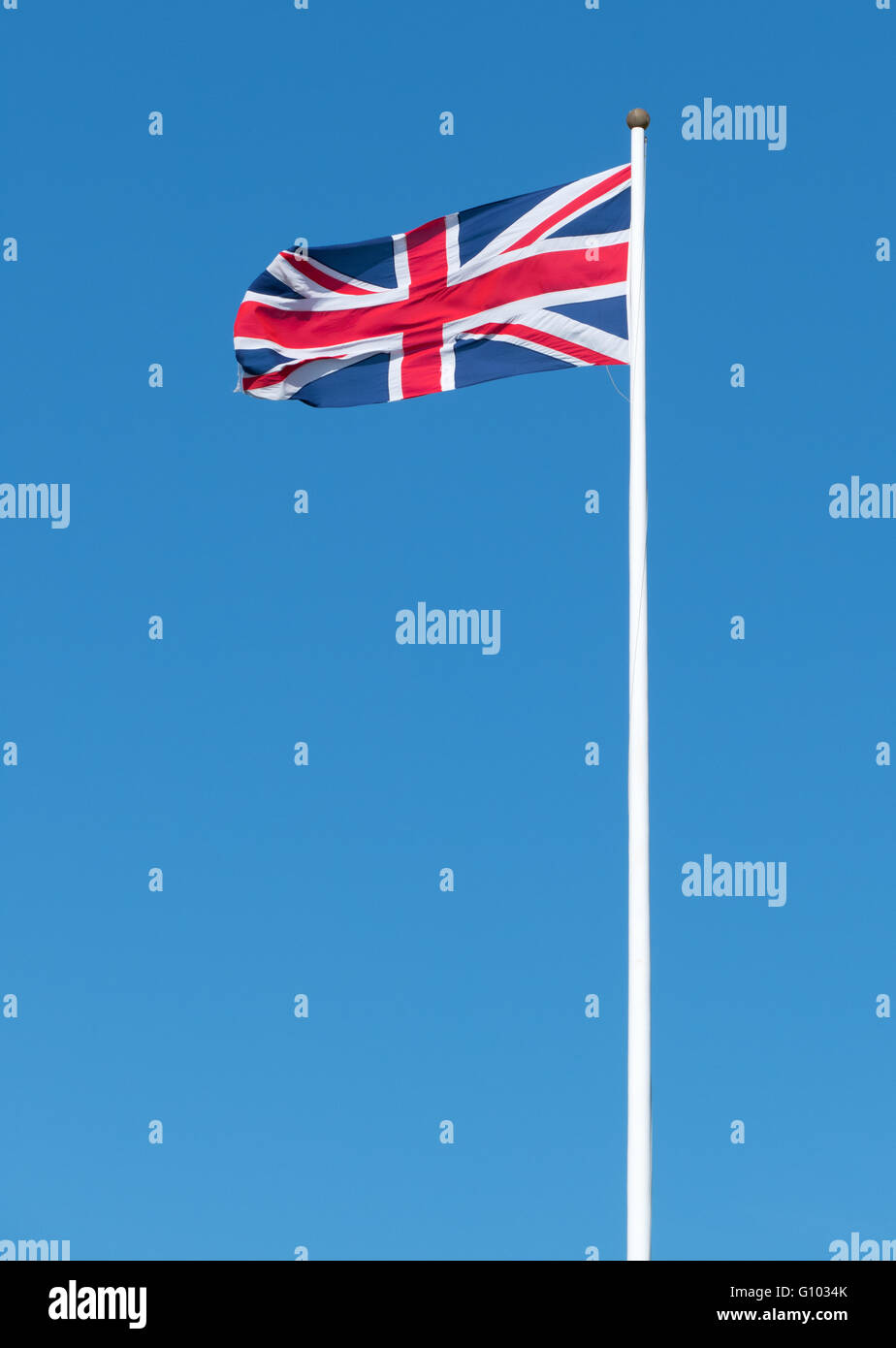 UK Union flag of Great Britain long flagpole blue sky. Stock Photo