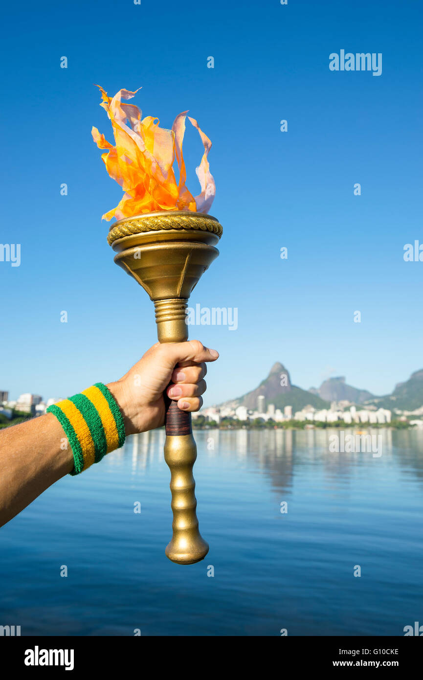 Hand of an athlete wearing Brazil colors sweatband holding ceremonial gold sport torch against Rio de Janeiro skyline at Lagoa Stock Photo