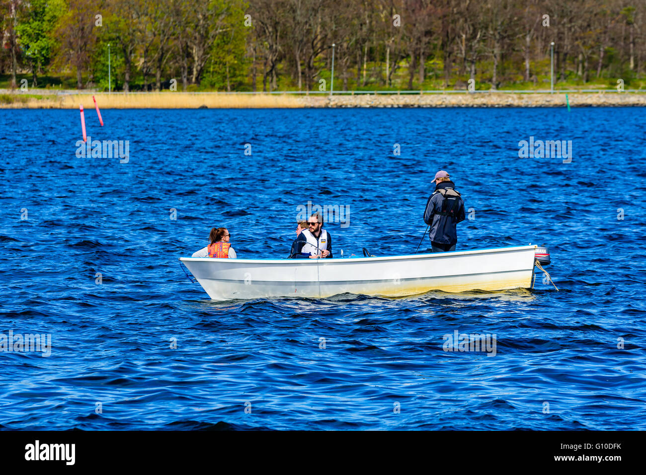 Karlskrona, Sweden - May 03, 2016: Four persons in a small open motorboat fishing at sea with coastline in background. Boat is m Stock Photo