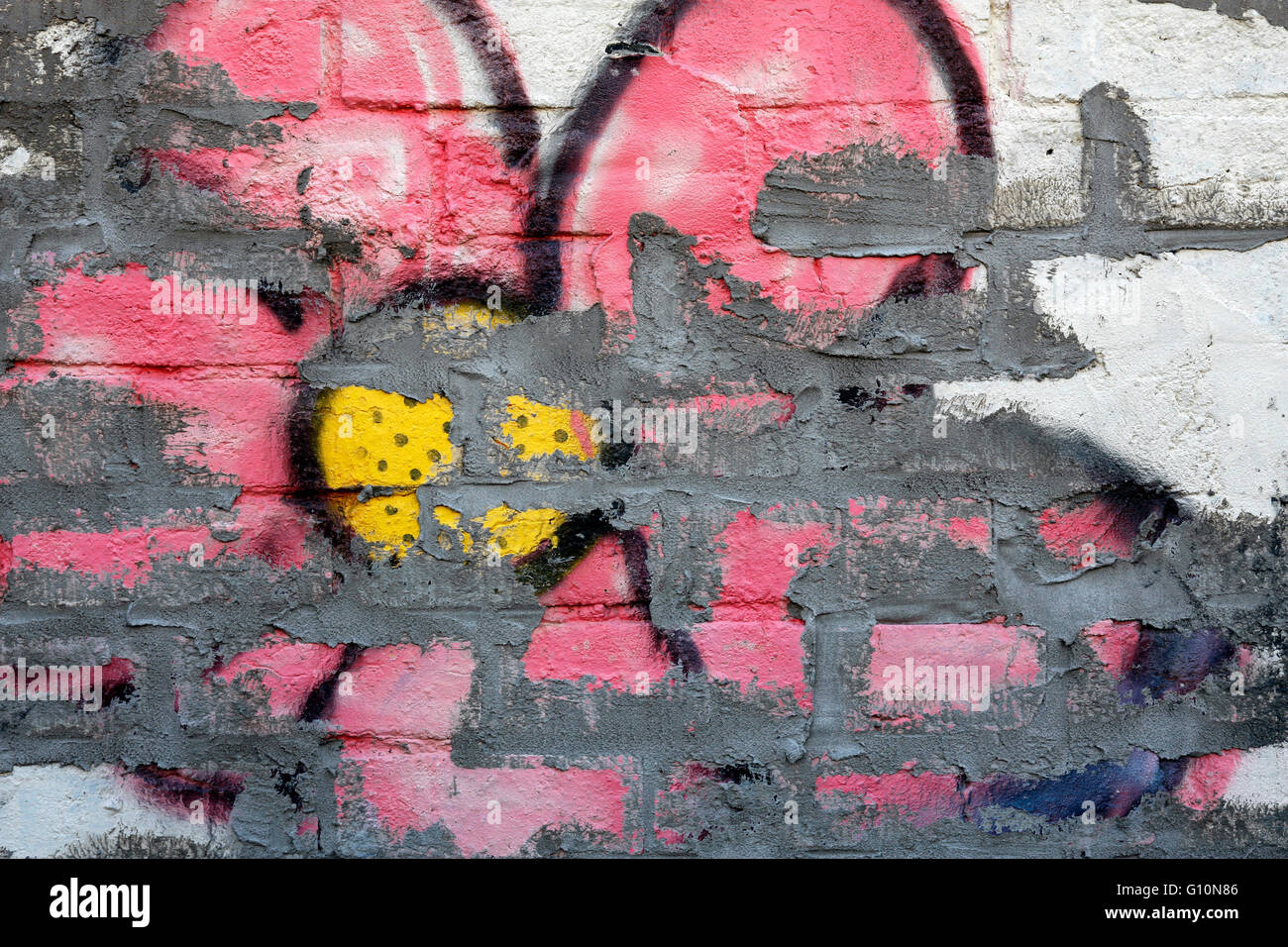 Pink and yellow graffiti flower on a white brick wall Stock Photo