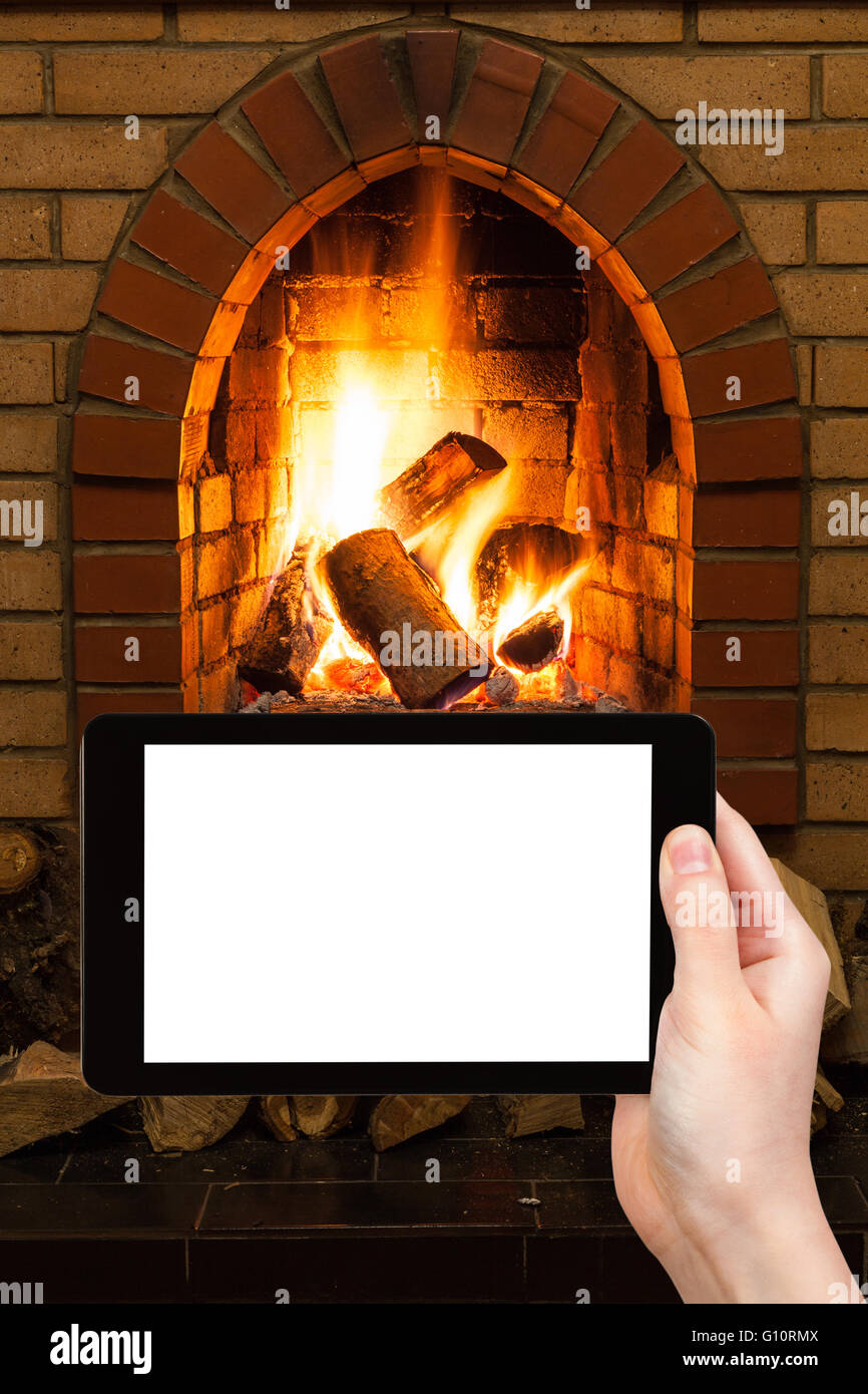 comfortable holiday concept - man photographs fireplace on tablet pc with cut out screen with blank place for advertising Stock Photo