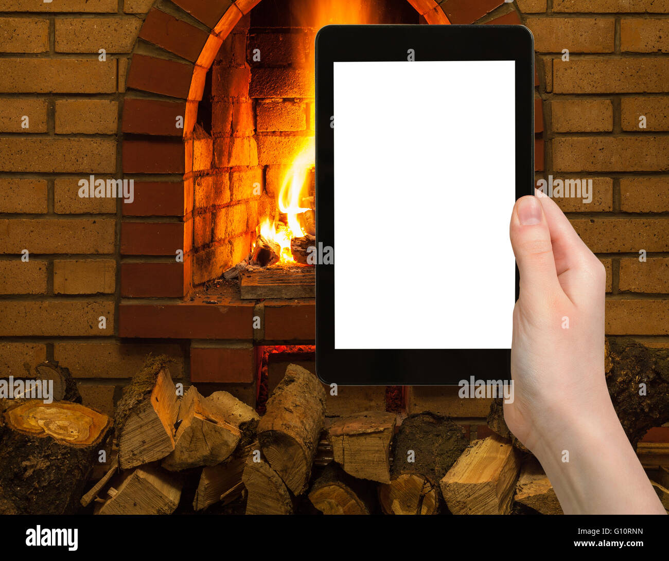 comfortable holiday concept - tourist photographs fireplace on tablet pc with cut out screen with blank place for advertising Stock Photo