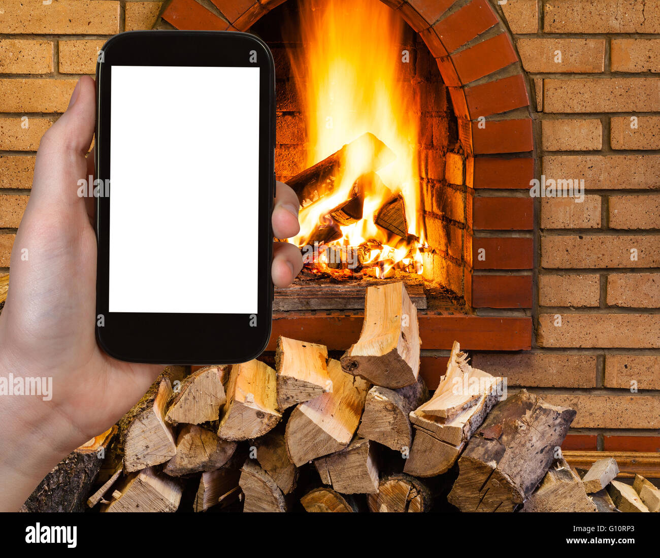 comfortable holiday concept - tourist photographs fireplace on smartphone with cut out screen with blank place for advertising Stock Photo