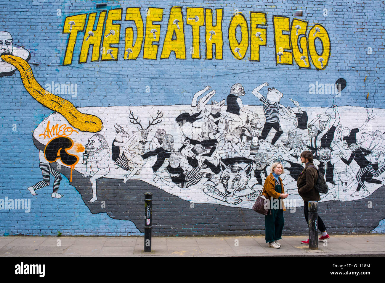 Hipster couple standing in front of a wall with a big graffiti with the writing 'The death of ego' on it. Stock Photo