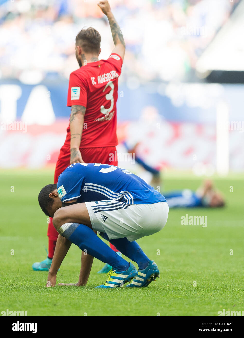 Gelsenkirchen, Germany. 07th May, 2016. Schalke's Joel Matip (FRONT) squats while Augsburg's Konstantinos Stafylidis celebrates in the background after the German Bundesliga soccer match between FC Schalke 04 and FC Augsburg in the Veltins Arena in Gelsenkirchen, Germany, 07 May 2016. Photo: GUIDO KIRCHNER/dpa (EMBARGO CONDITIONS - ATTENTION - Due to the accreditation guidelines, the DFL only permits the publication and utilisation of up to 15 pictures per match on the internet and in online media during the match)/dpa/Alamy Live News Stock Photo