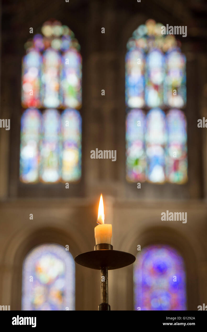 Single lit prayer candle in front of a modern stained glass window in