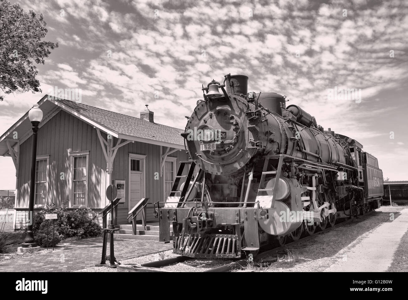 Old railroad steam engine by train station. Stock Photo