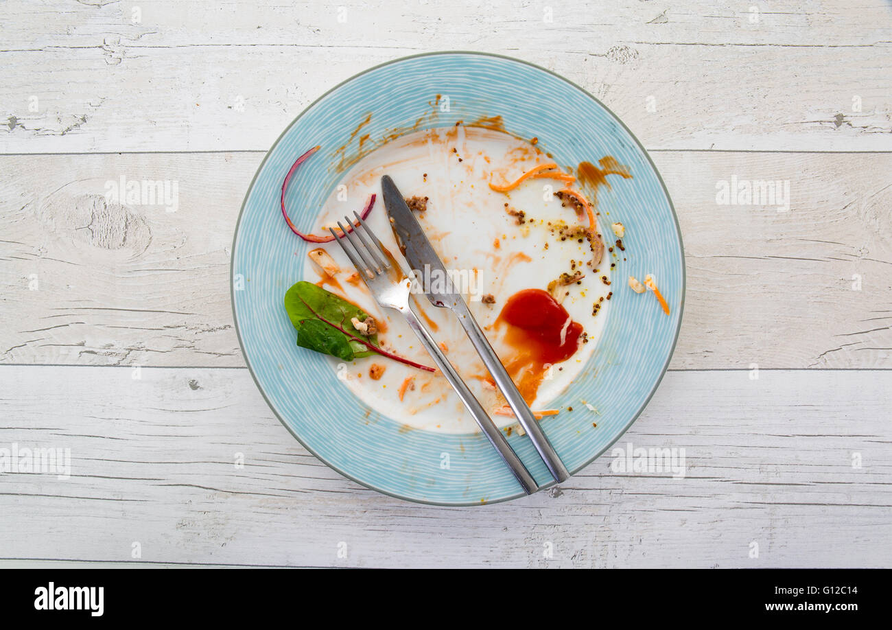 Overhead shot of an empty plate with leftovers from a meal on a white wooden background Stock Photo