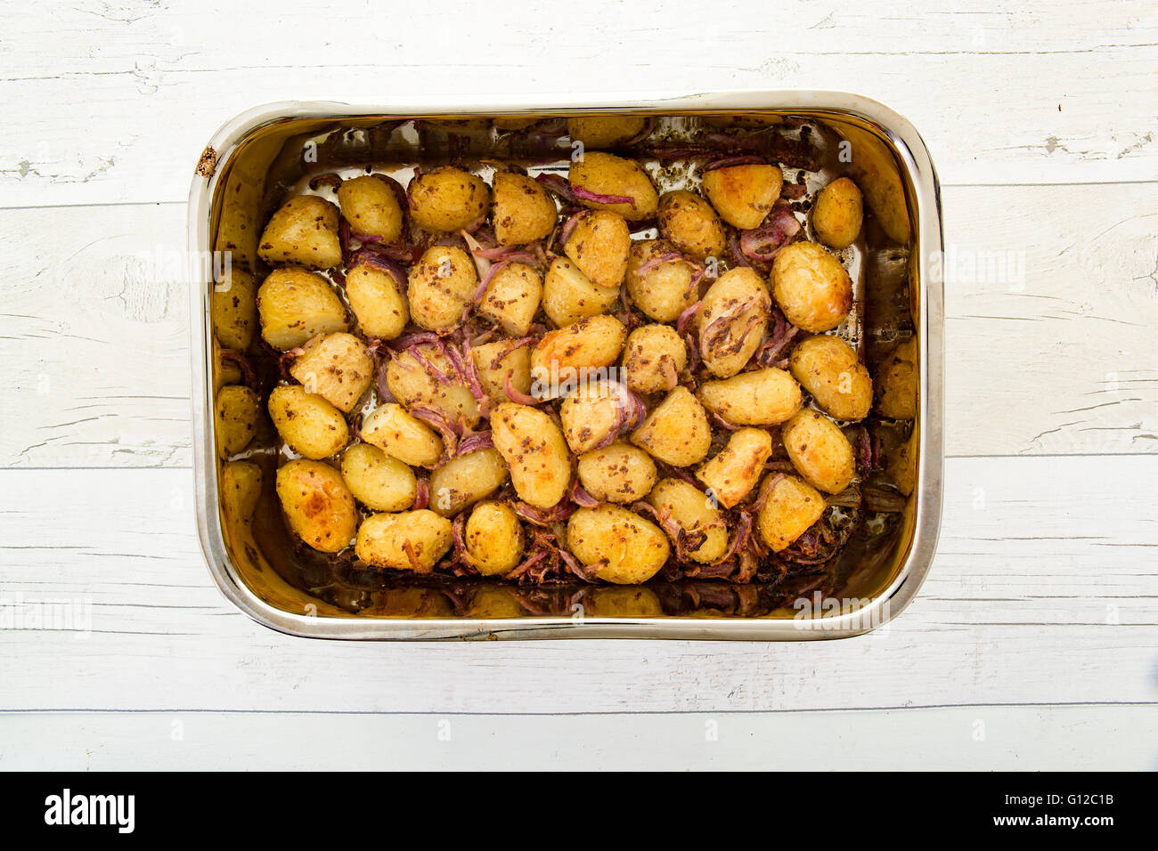 mustard crusted new potatoes with shallots in a dish on a rustic wooden table Stock Photo