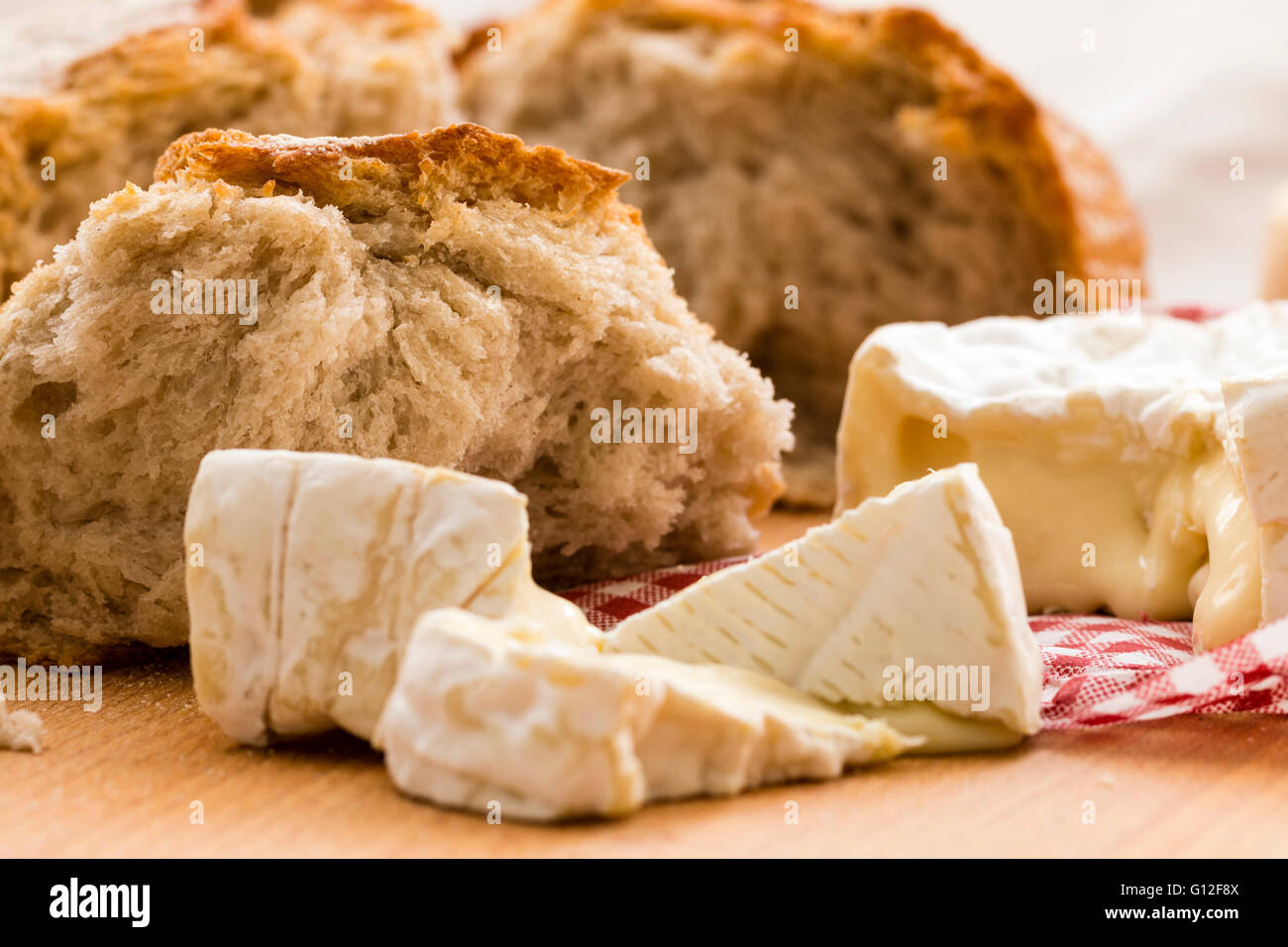 Round Camembert cheese, pieces cut out, on wooden chopping board with