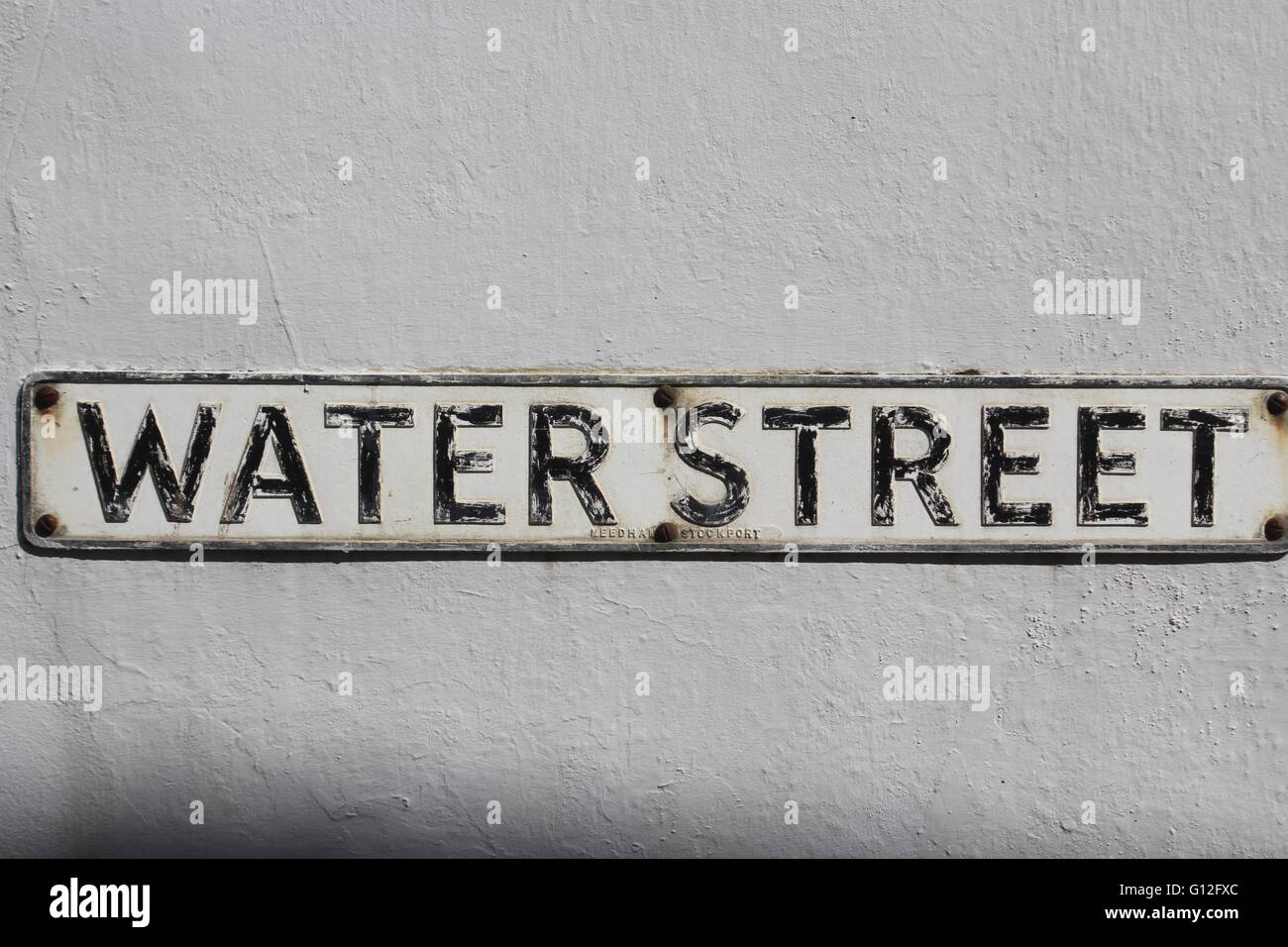 Old metal street sign with black letters on a white background saying 'Water Street' mounted on a white painted stone wall. Stock Photo