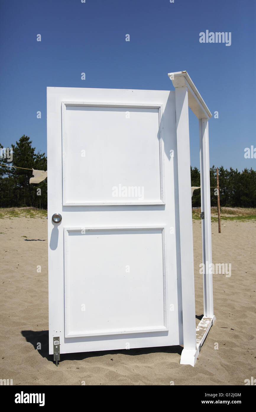 White door on the sand against blue sky Stock Photo