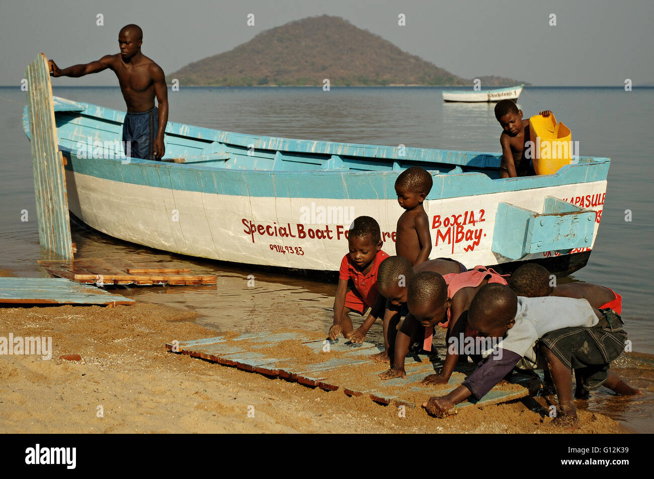 Man washing a boat with kids on the shore of Lake Malawi at Cape Maclear Stock Photo