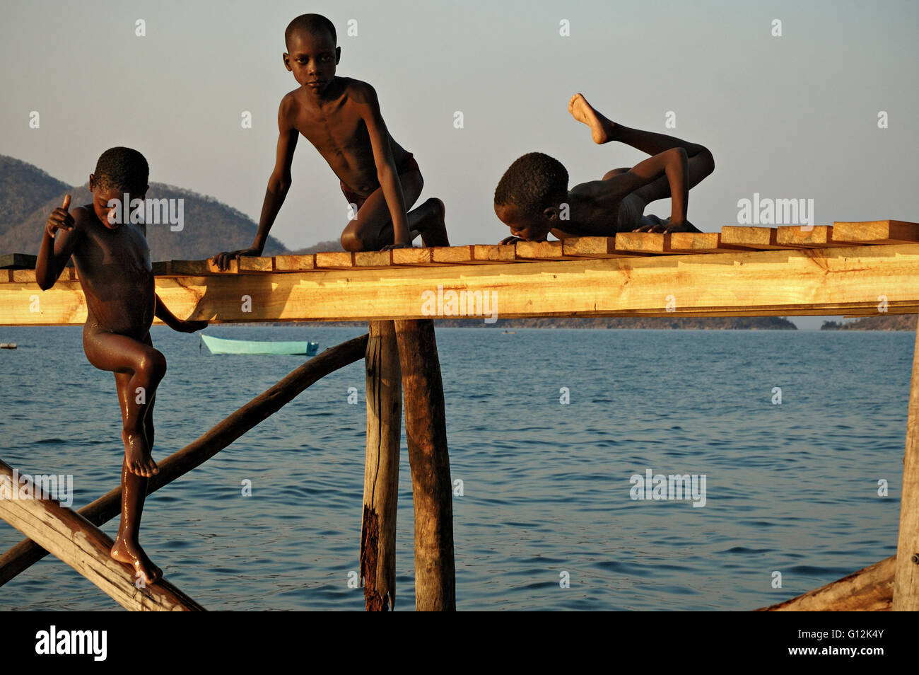 Three boys playing on a pier for boats above Lake Malawi, Cape Maclear Stock Photo