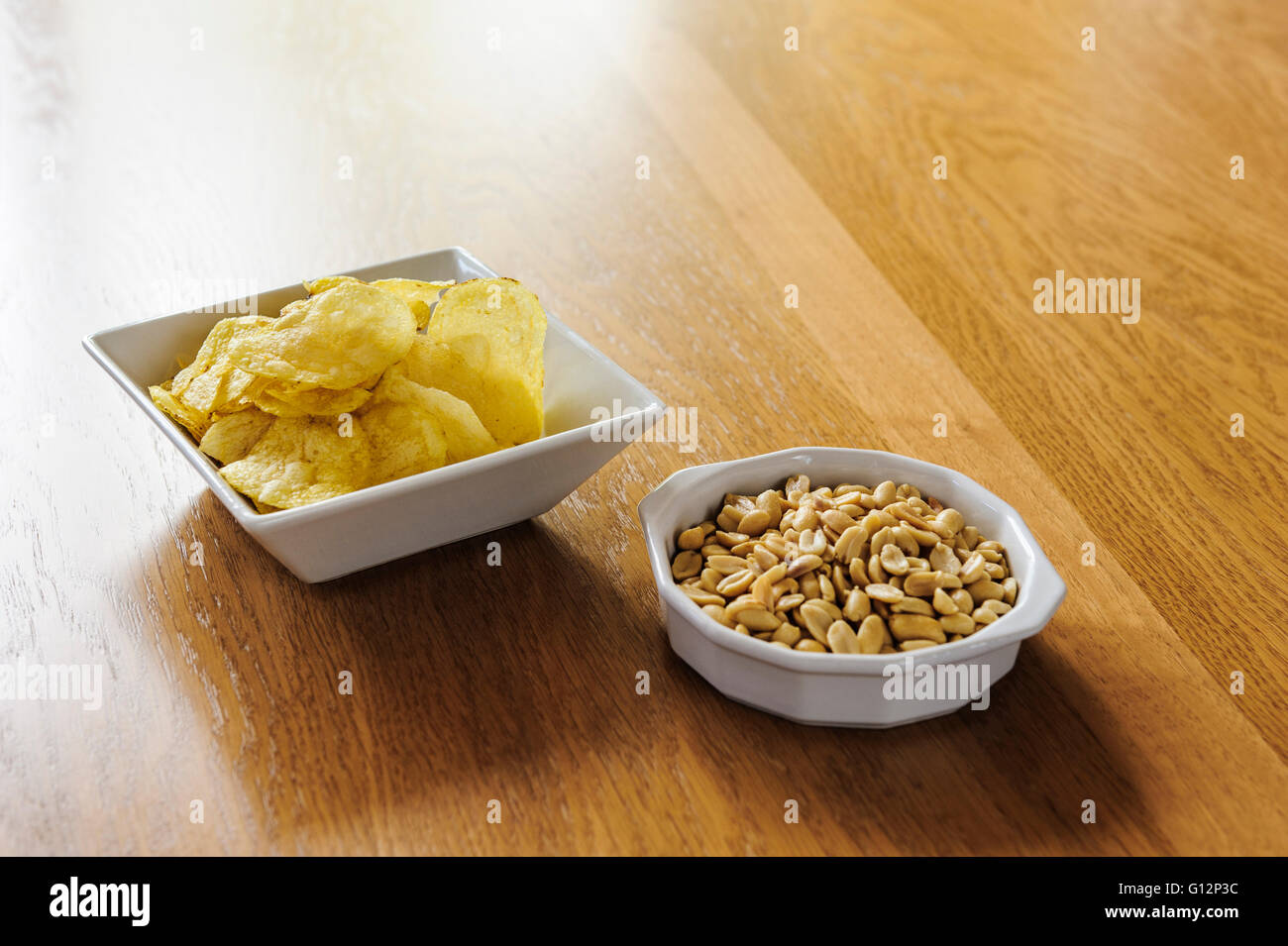 Bowls of crisps and peanuts on an oak dining table. Stock Photo