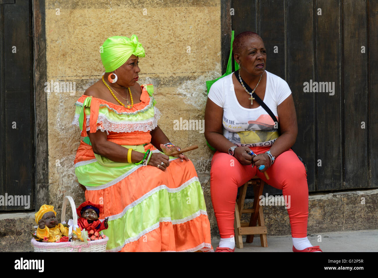 A Cuban doll seller wearing traditional costume and smoking a cigar relaxes with a companion in Old Havana, Havana, Cuba Stock Photo