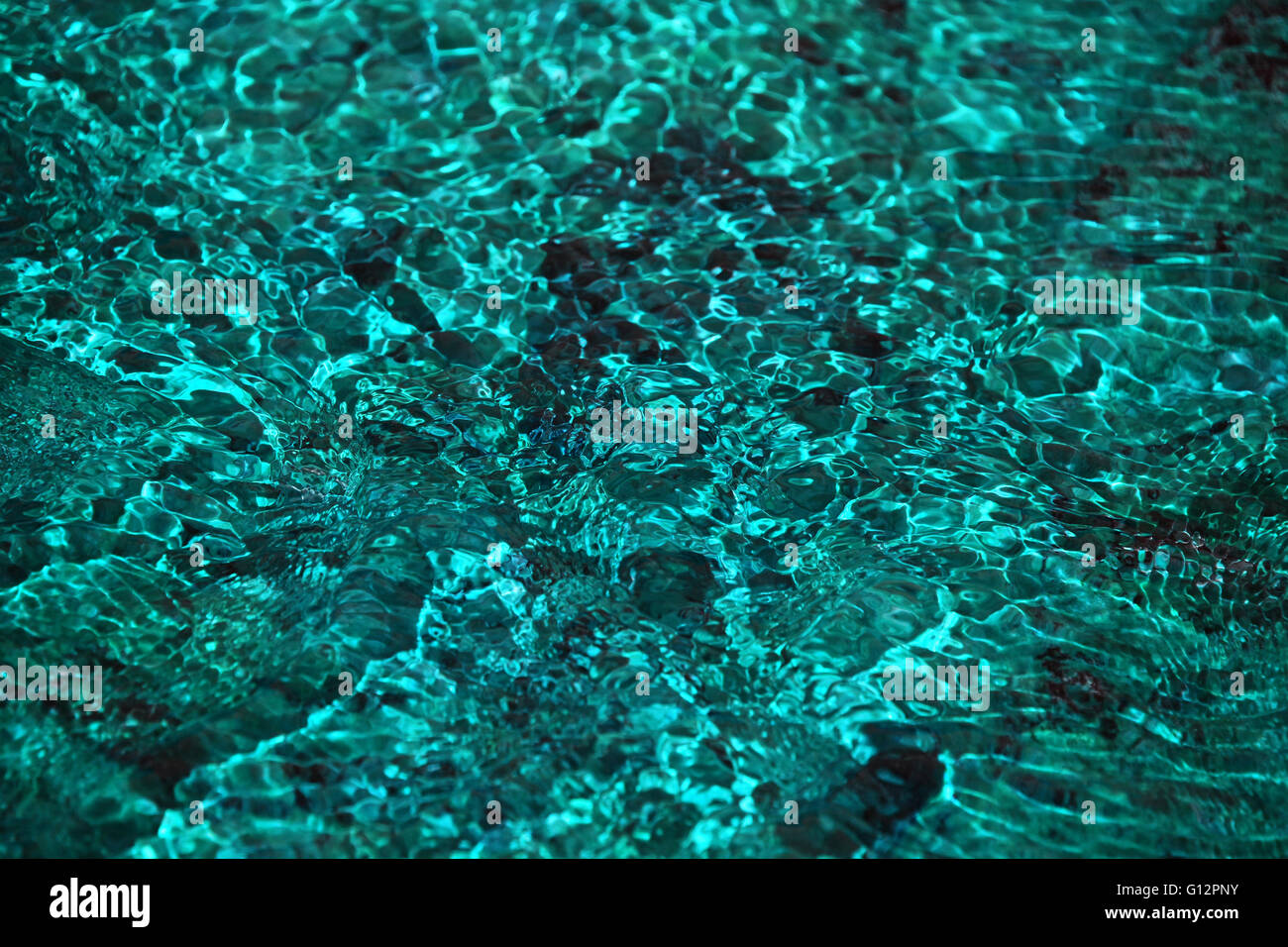 Running water teal blue color stream deflection flowing over stones texture background Stock Photo