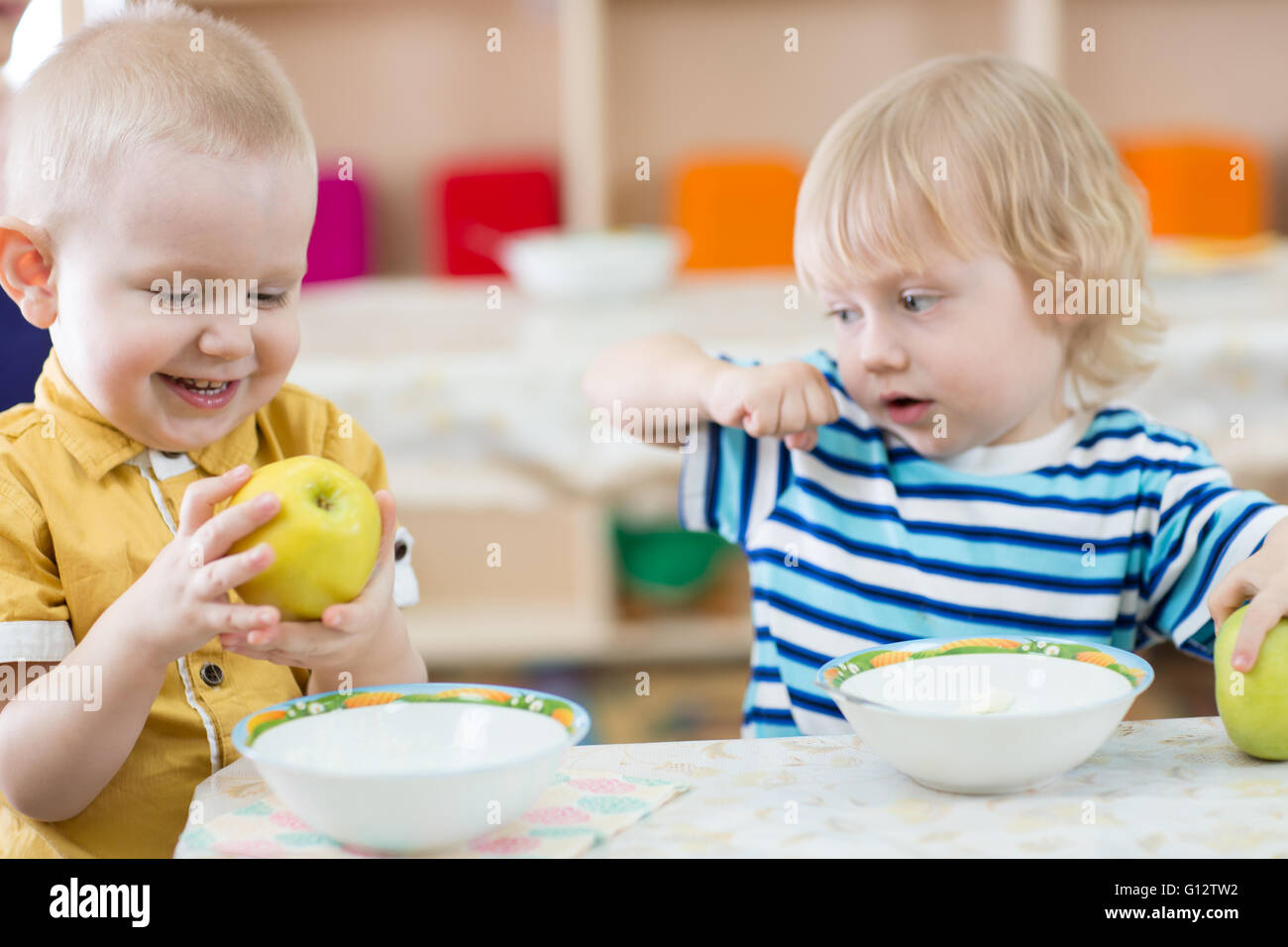 Funny smiling kid eating apple in kindergarten Stock Photo
