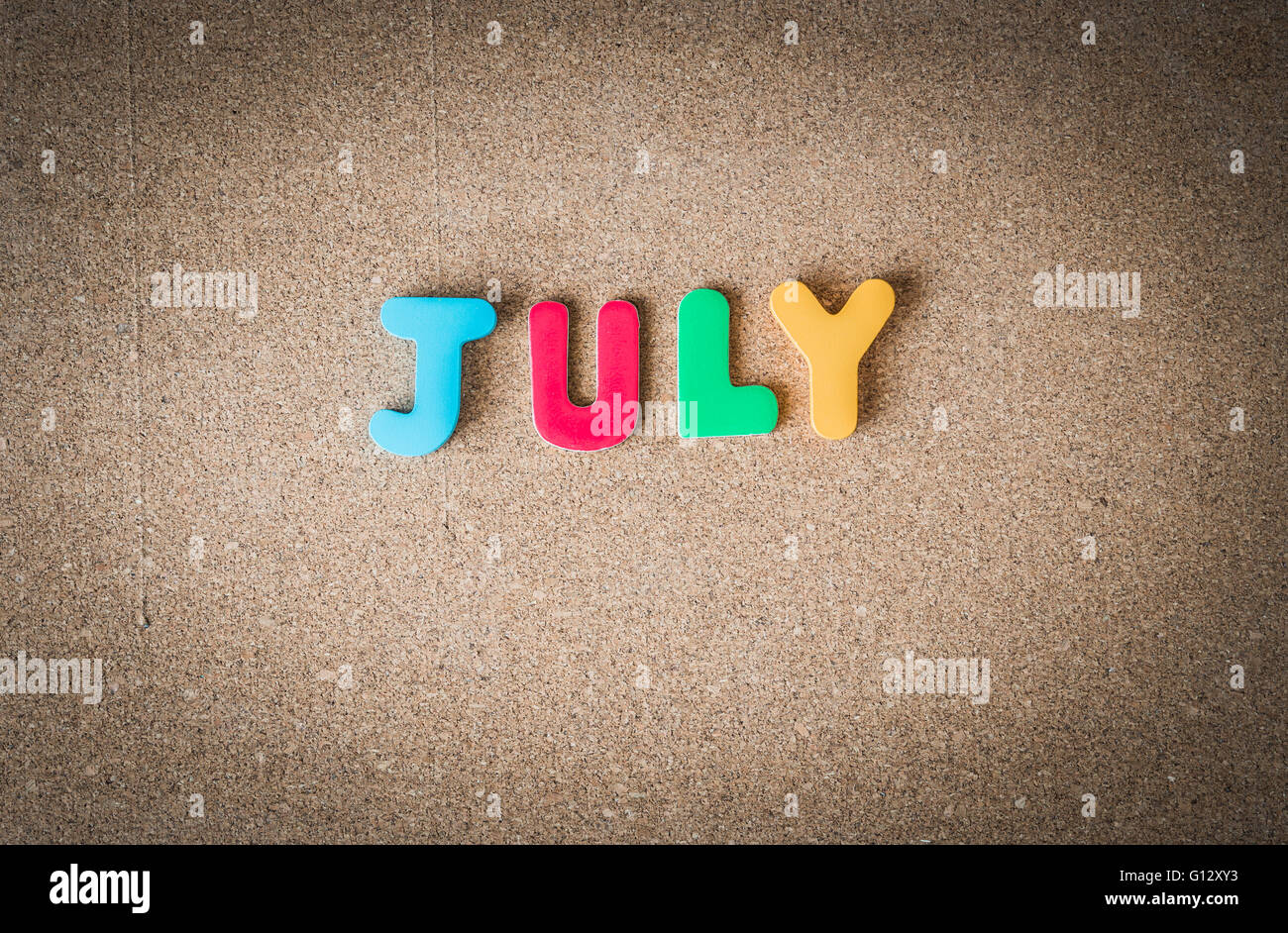 Colorful wooden word JULY on cork board with selective focus Stock