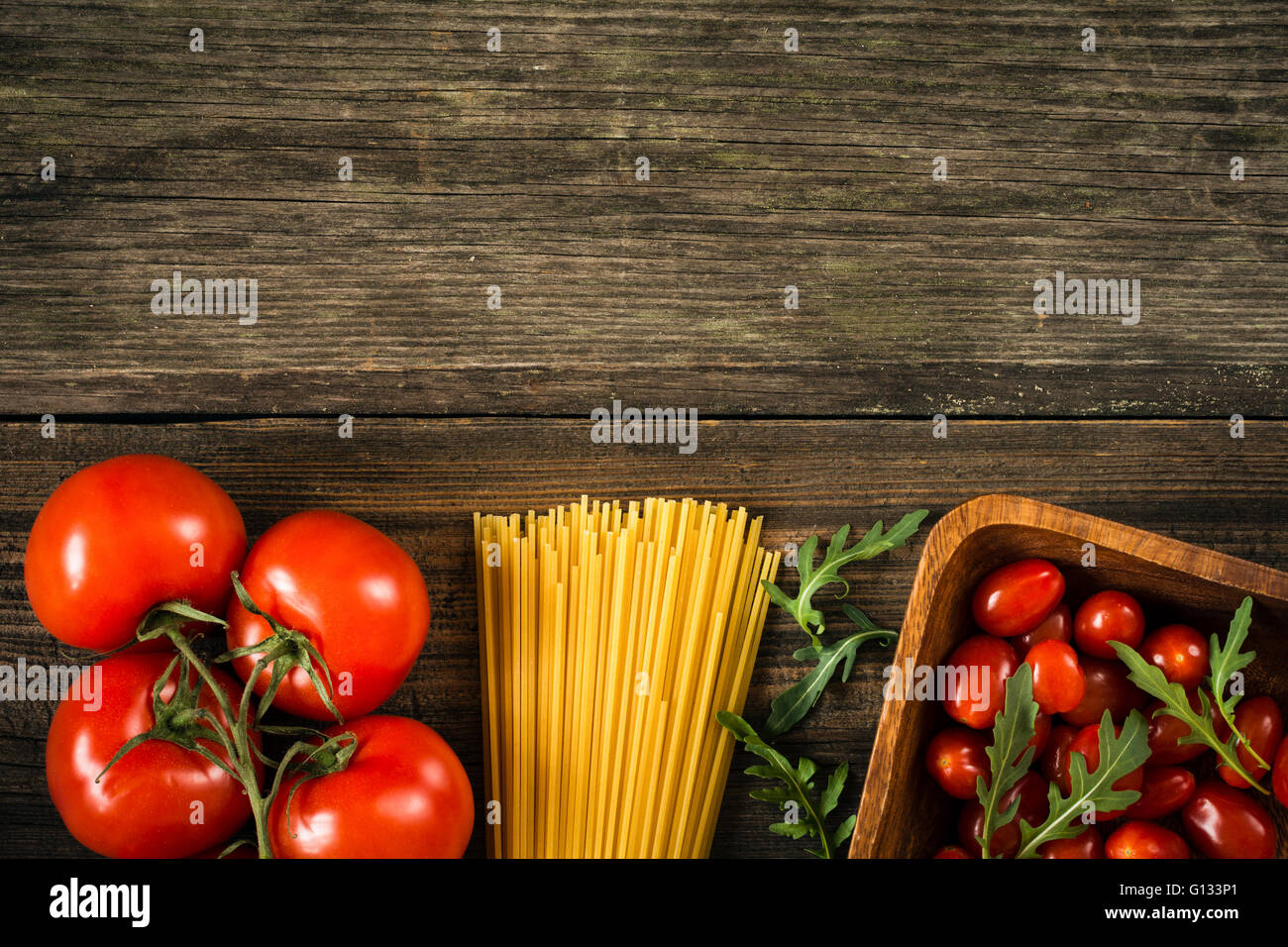 Italian food background / cooking ingredients background. Dry pasta, tomatoes, olive oil and salad leaves on wooden backdrop Stock Photo