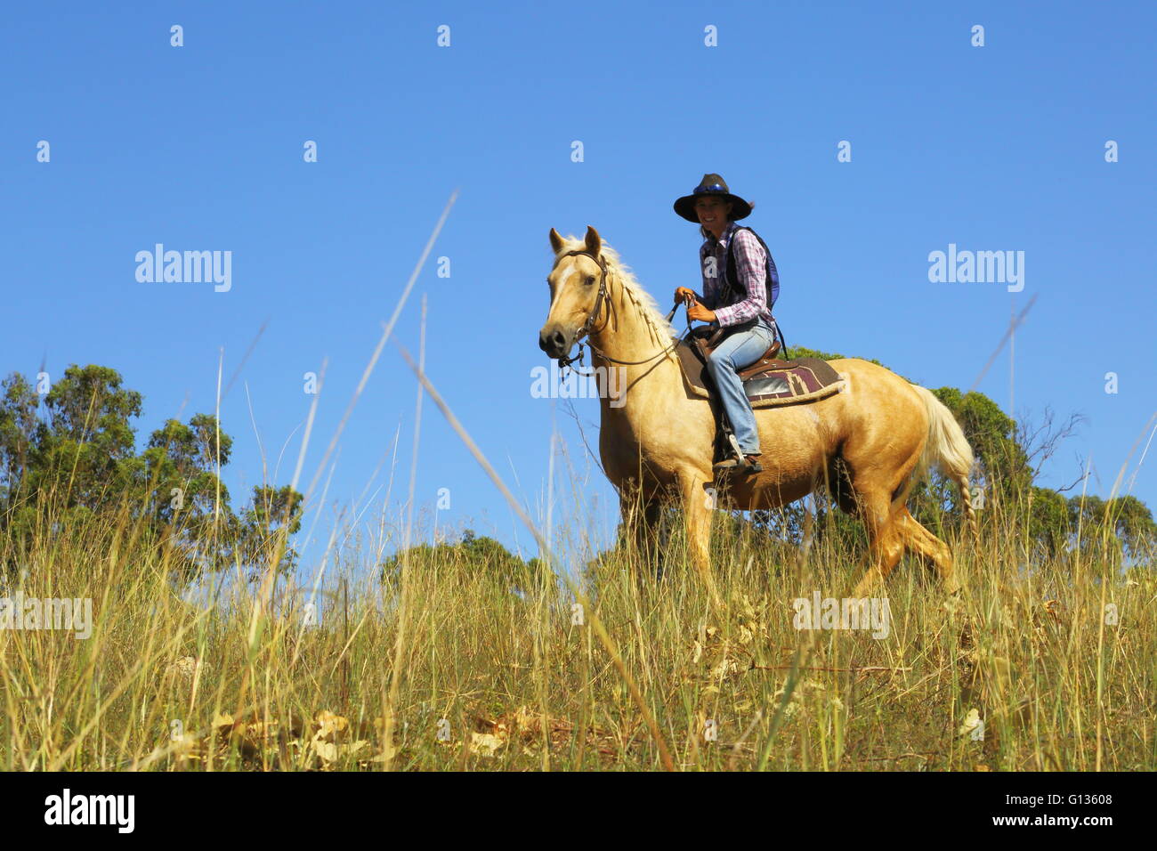 A young cowgirl in her late teens or early twenties rides her horse under a big blue sky. Stock Photo