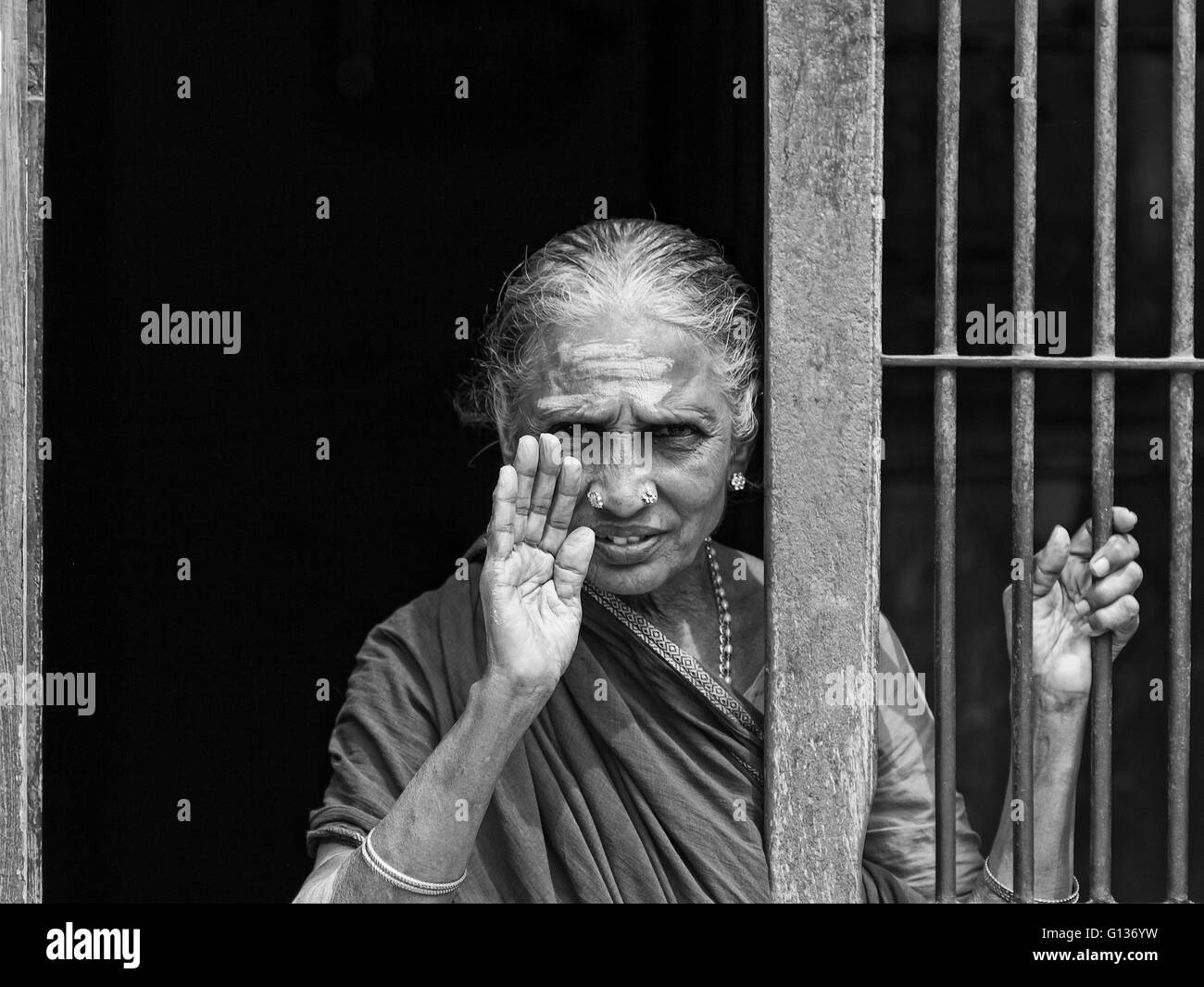 Indian lady waving through a barred entrance outside of the Kapaleeshwarar Temple, Mylapore, Chennai, Tamil Nadu, India Stock Photo