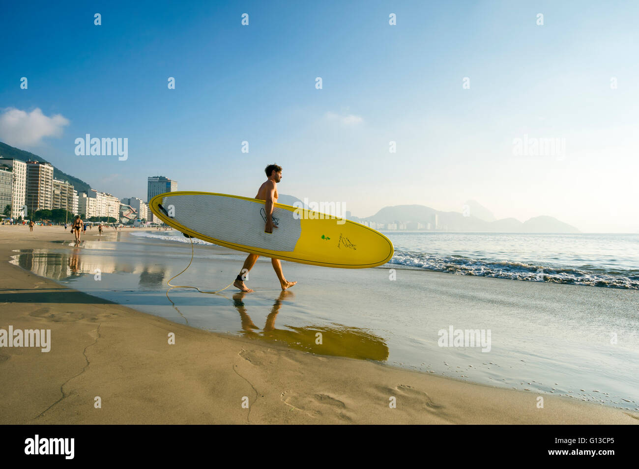 RIO DE JANEIRO - APRIL 5, 2016: A young Brazilian man carries a stand up paddle longboard surfboard on Copacabana Beach. Stock Photo