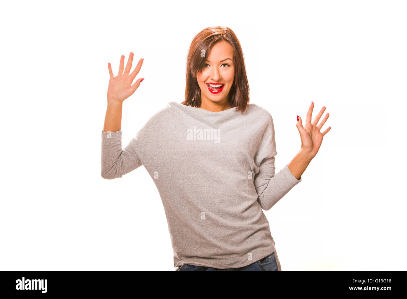 Beautiful happy young woman standing with hands up, wearing jeans and grey blouse. Stock Photo
