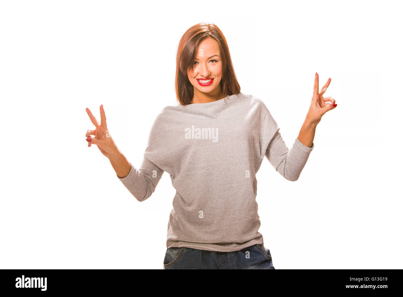 Beautiful happy young woman standing with hands up, wearing jeans and grey blouse. Stock Photo