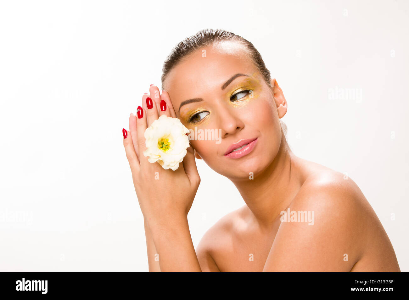 Gold make up. Brown sleek hair beautiful woman with white flower in hands close to face. Stock Photo