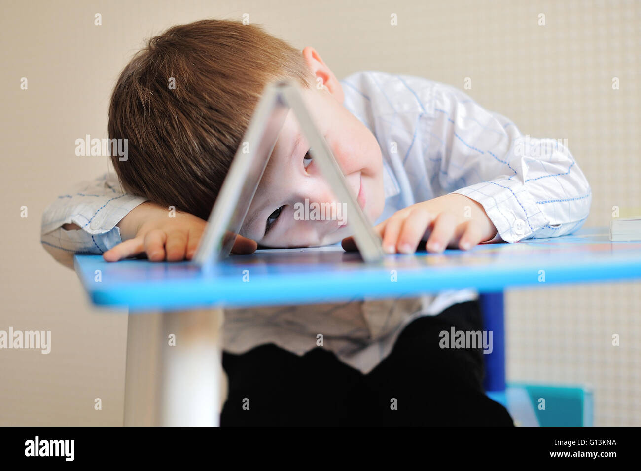 Young schoolboy playing with books and smiling as he sits at his desk in classroom Stock Photo