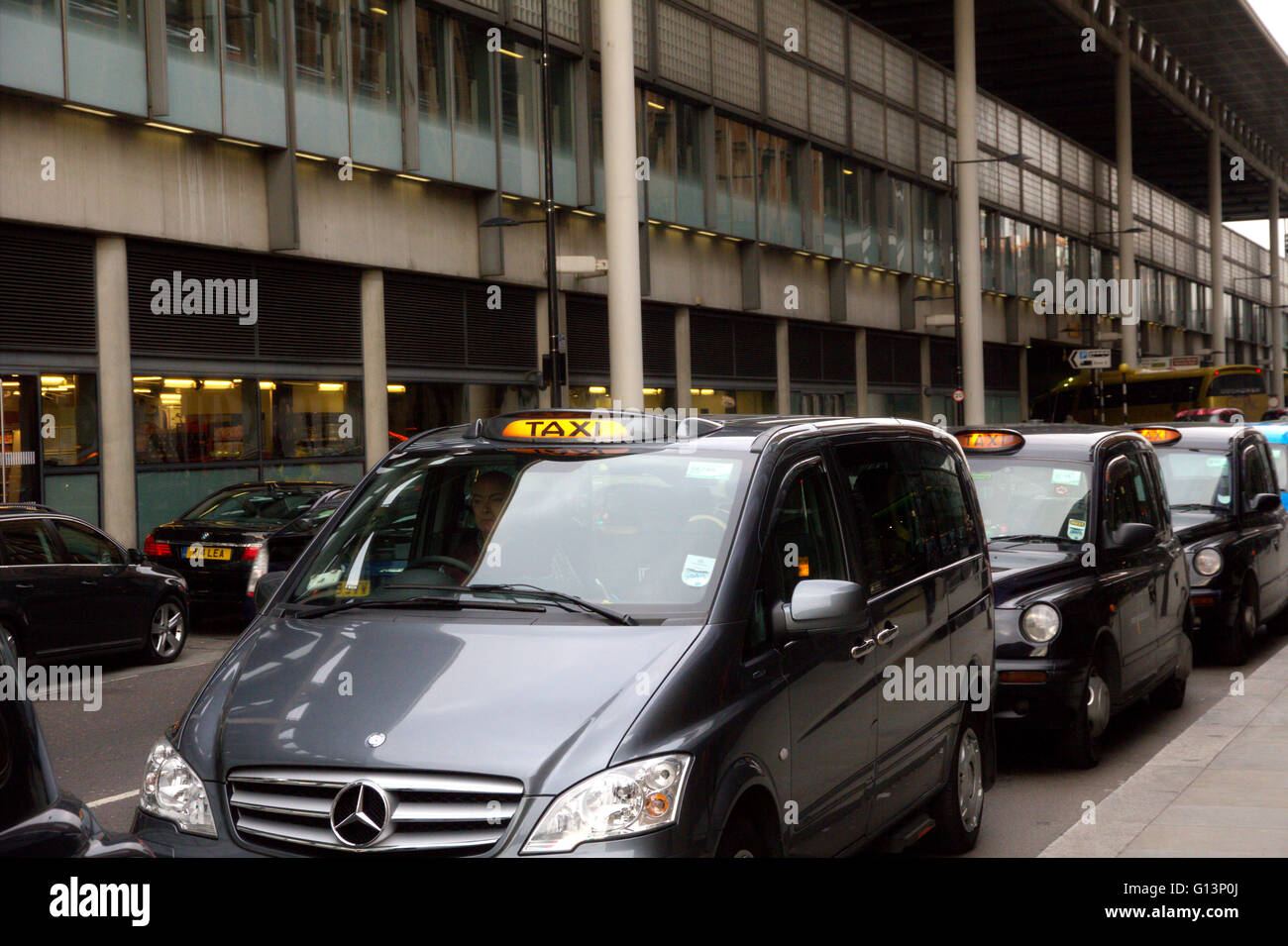 A queue of London black cab taxis in a row at a taxi rank, waiting to pick up passengers near Kings Cross station with for hire light illuminated Stock Photo