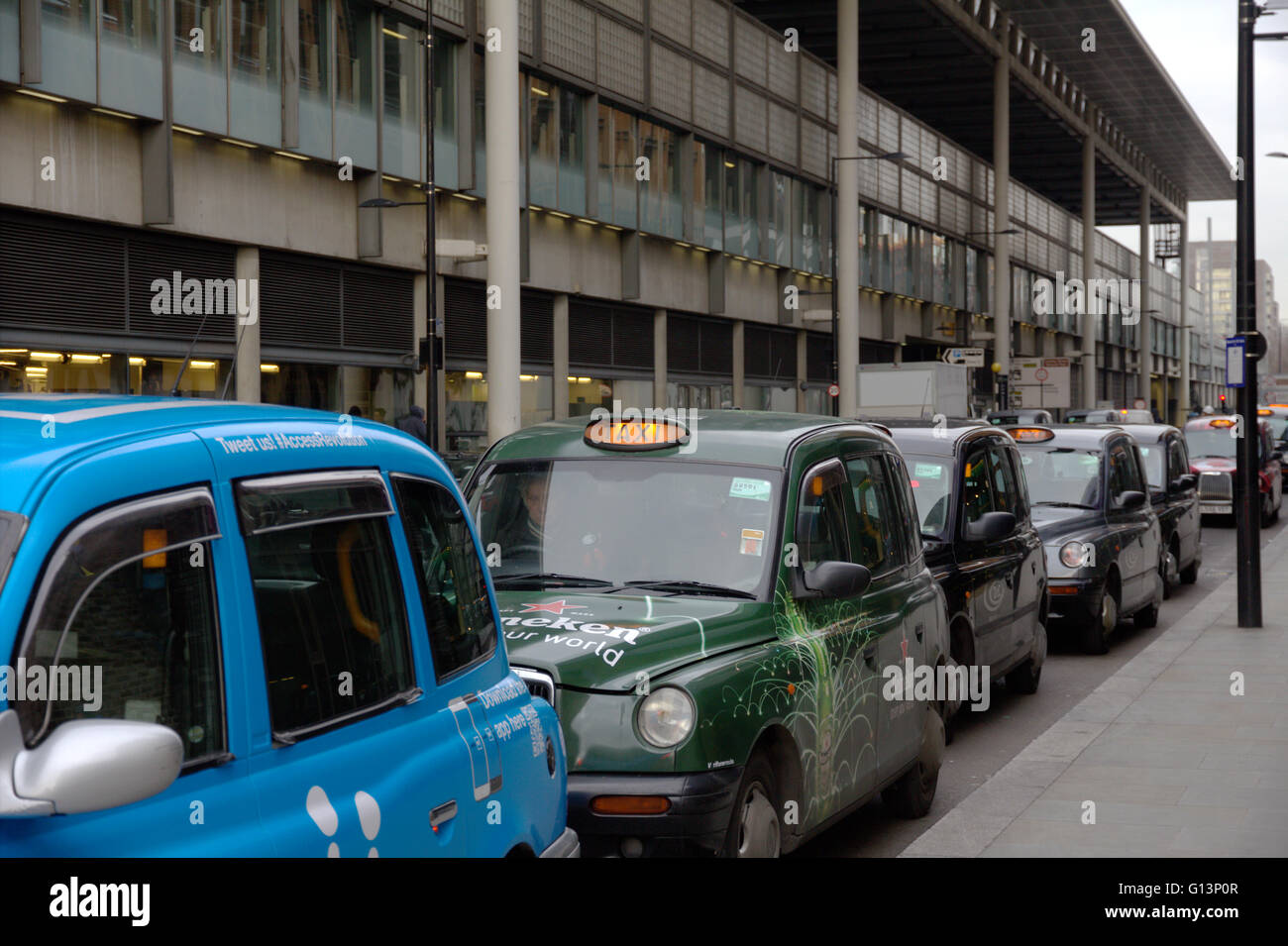 A queue of London black cab taxis in a row at a taxi rank, waiting to pick up passengers near Kings Cross station with for hire light illuminated Stock Photo