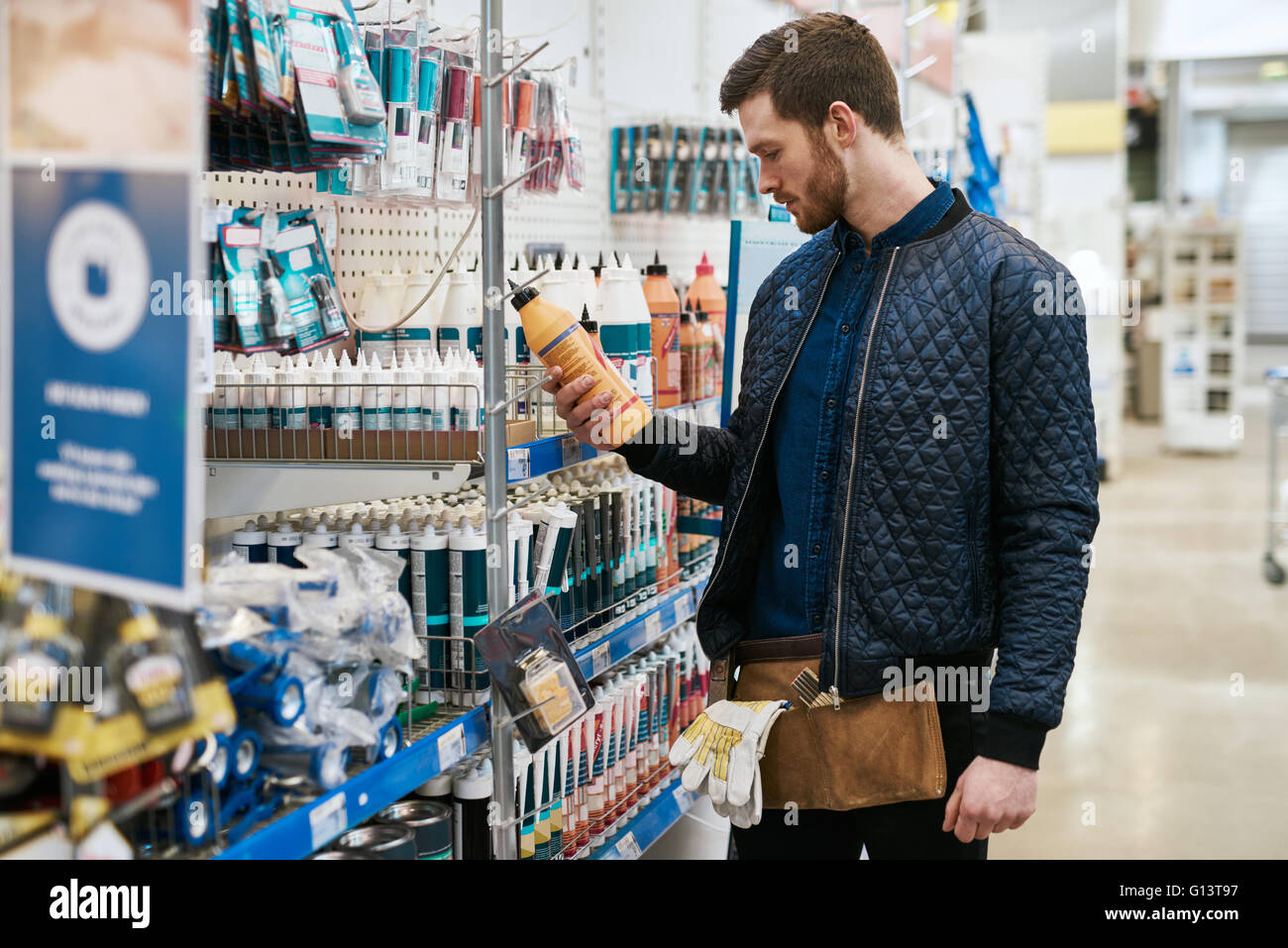 Handyman selecting a product at a hardware store standing reading the label on a container, profile view Stock Photo