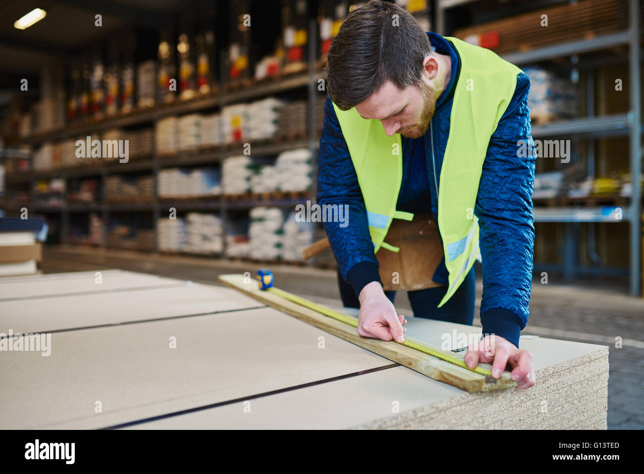 Handyman working in warehouse measuring a piece of wood Stock Photo