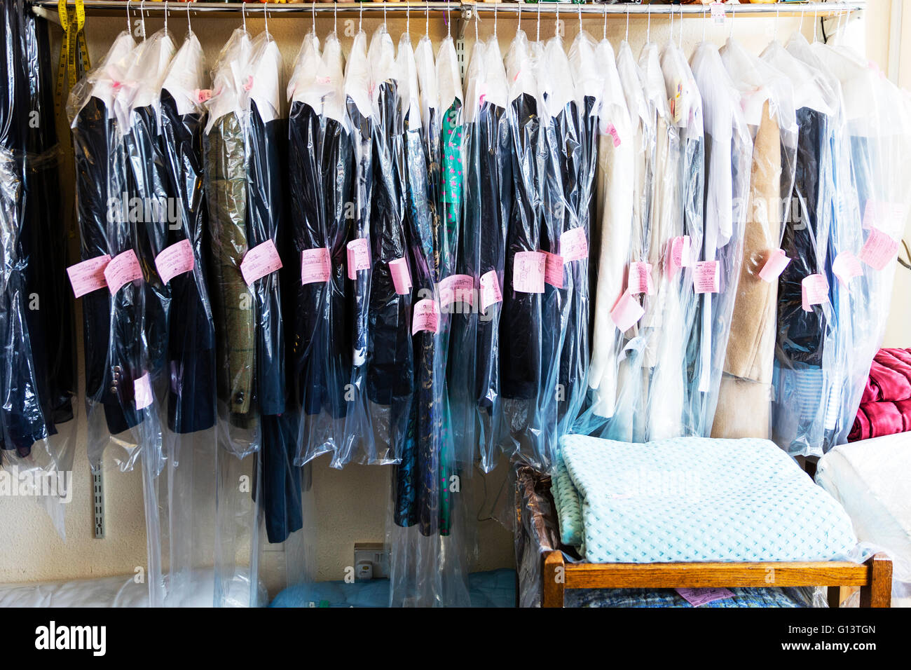 Dry cleaning clothes cleaned ready for collection tickets of customers on protective cover UK England English towns Stock Photo