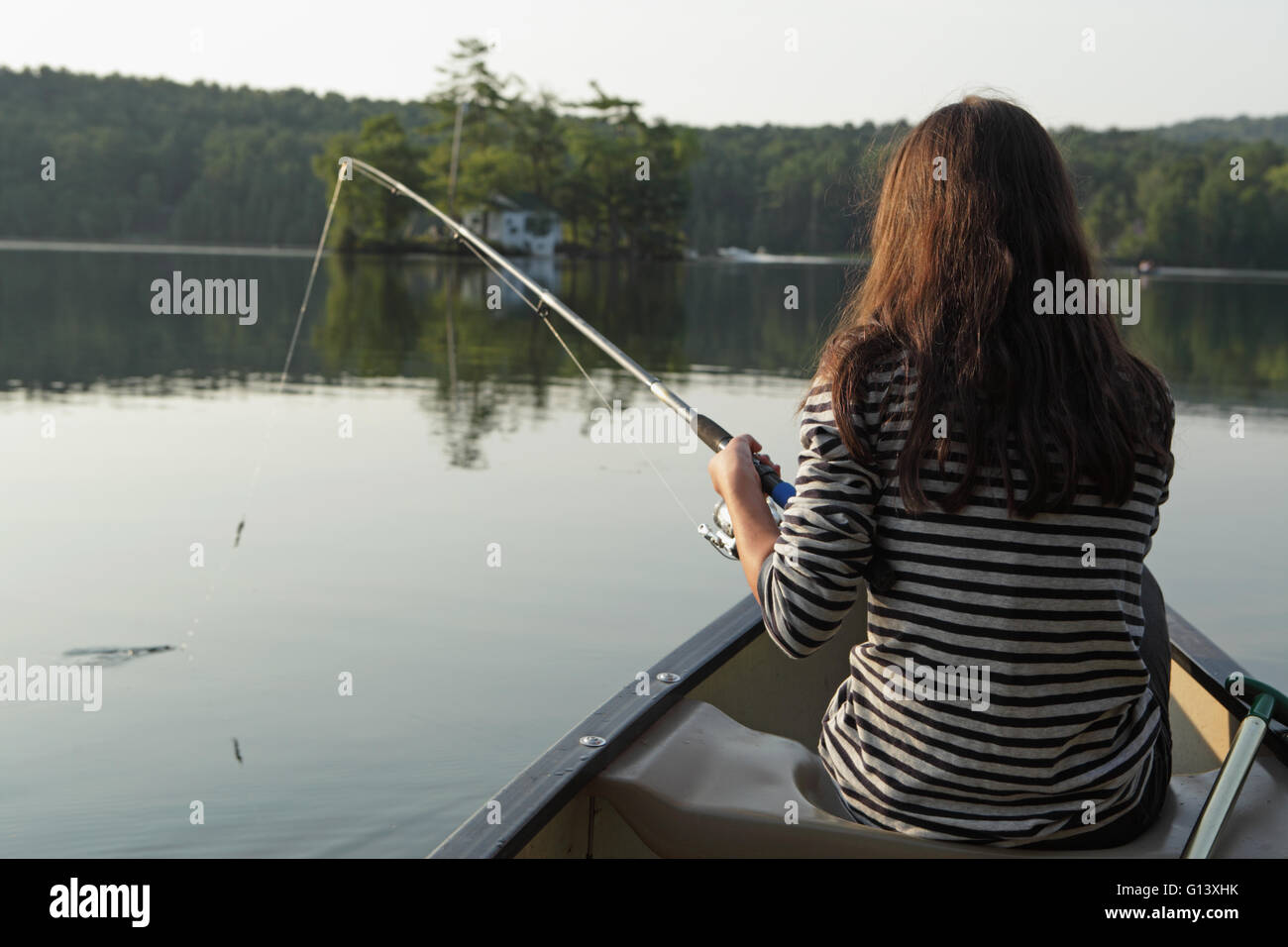 Young girl fishing from a canoe in a lake in western Vermont Stock Photo