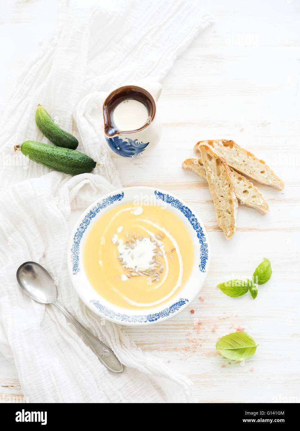 Pumpkin soup with cream, fresh basil, cucumbers and bread in vintage ceramic plate over white wooden background, top view Stock Photo