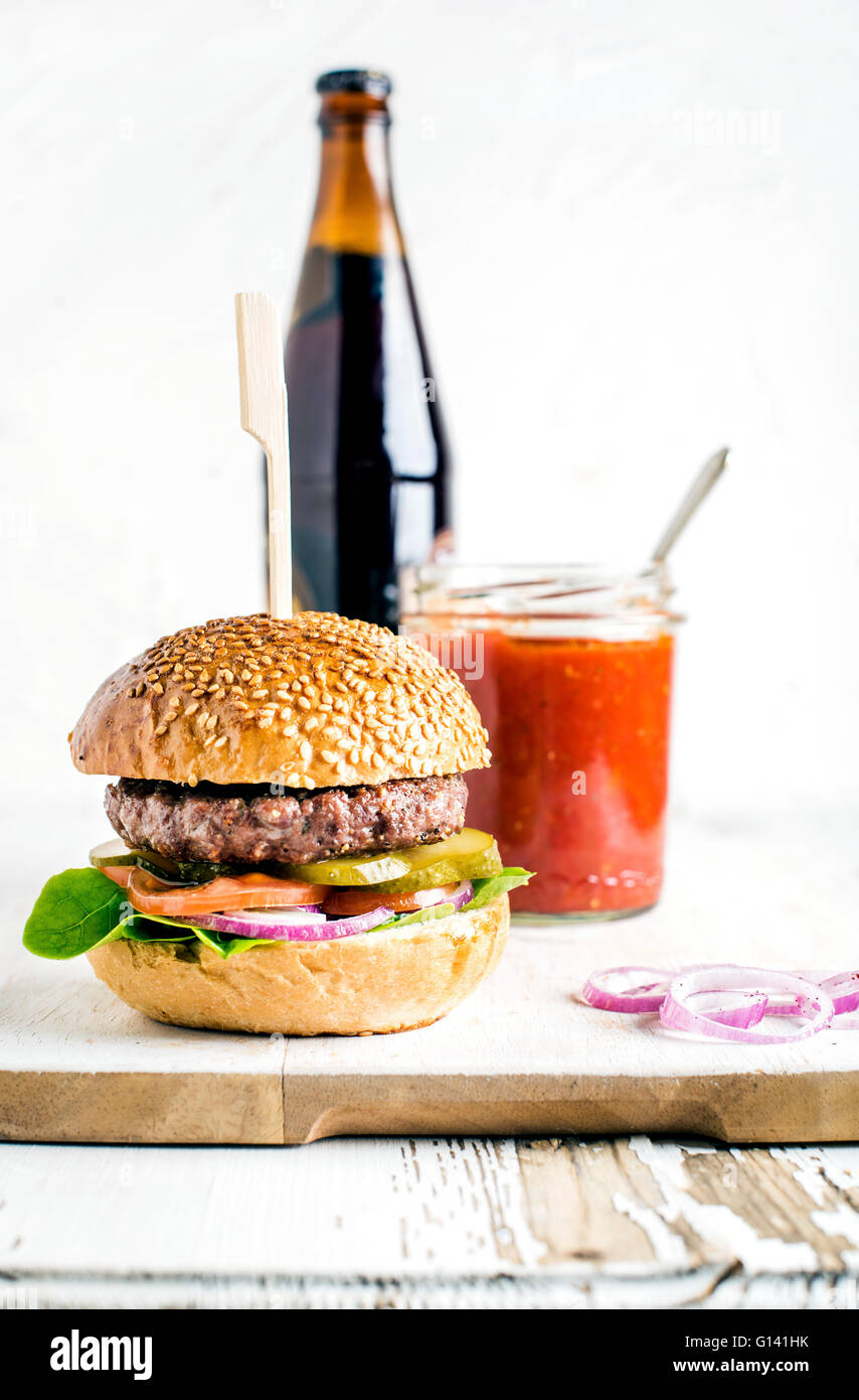 Fresh homemade burger on wooden serving board with spicy tomato sauce and bottle of dark beer. White  background, selective focu Stock Photo