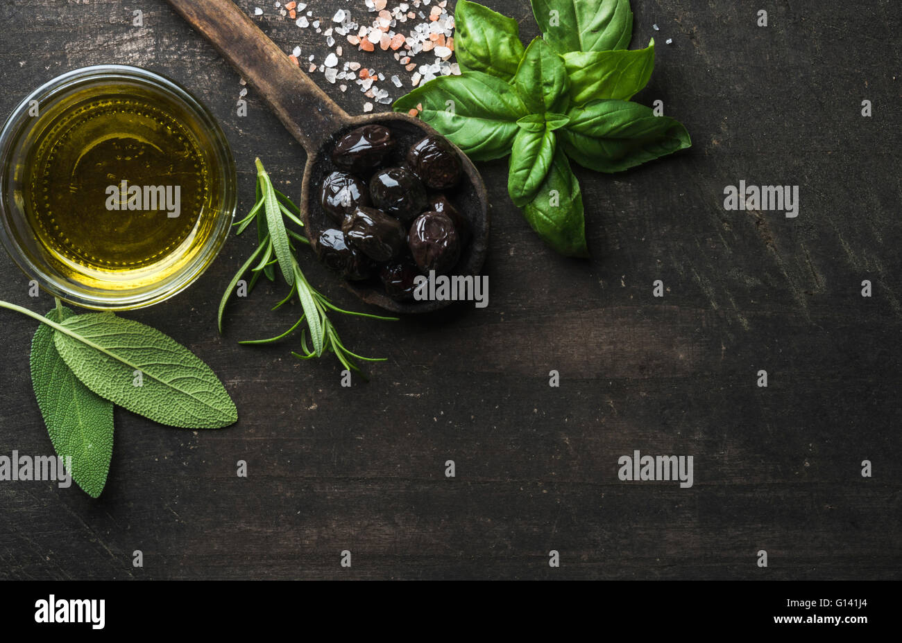 Greek black olives, fresh green sage, rosemary, basil herbs, salt and oil on dark rustic wooden background.  Top view, copy spac Stock Photo