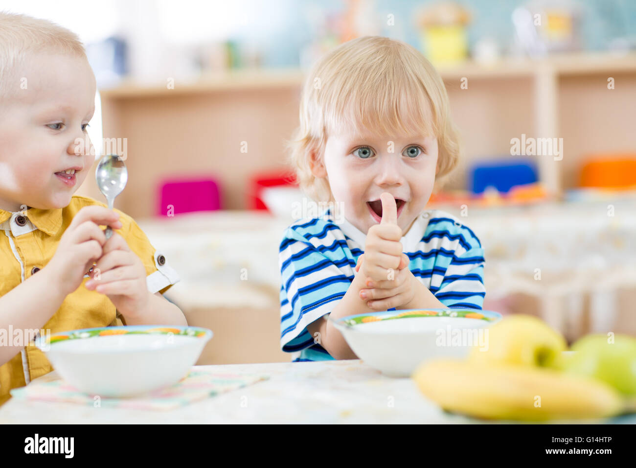 Kid eating in kindergarten and showing thumbs up Stock Photo