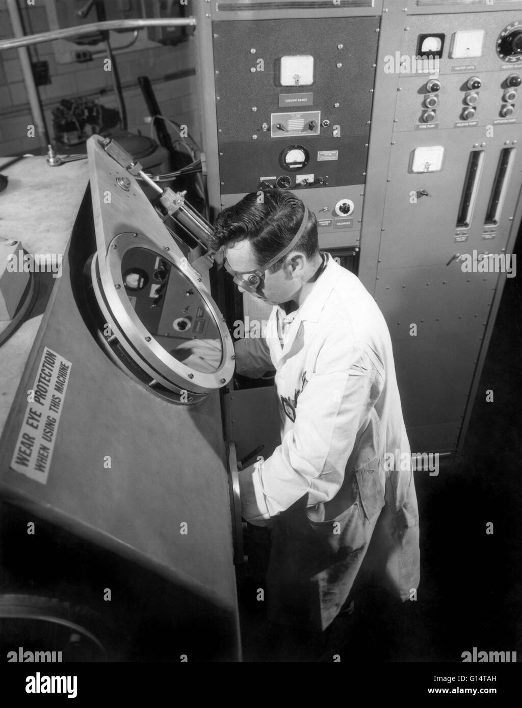 Peering through the port of a vacuum welding box, a technician for Westinghouse Electric Corporation's atomic power department guides equipment that is capping the end of an alloy tube which will contain atomic fuel for a power reactor. The tube, made of Stock Photo