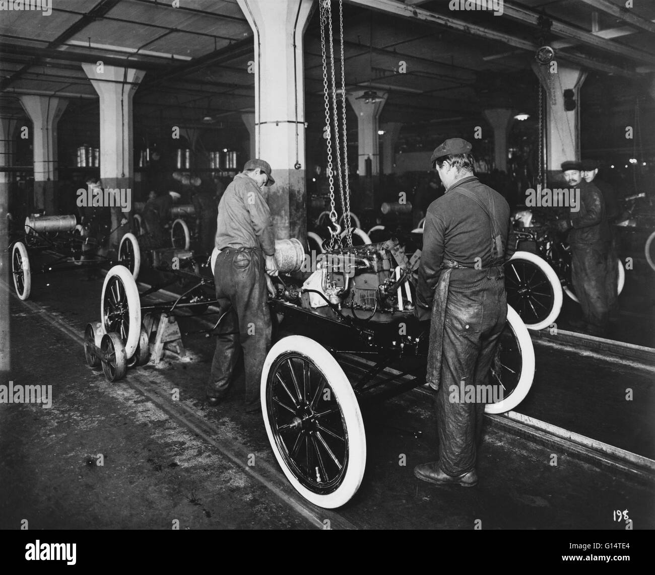 A 'push type' assembly line at the Highland Park plant in Michigan. The above photograph shows a Model T engine being dropped into place by use of an overhead block-and-tackle. The picture was taken in early 1913 and it shows how the rear wheels were crad Stock Photo