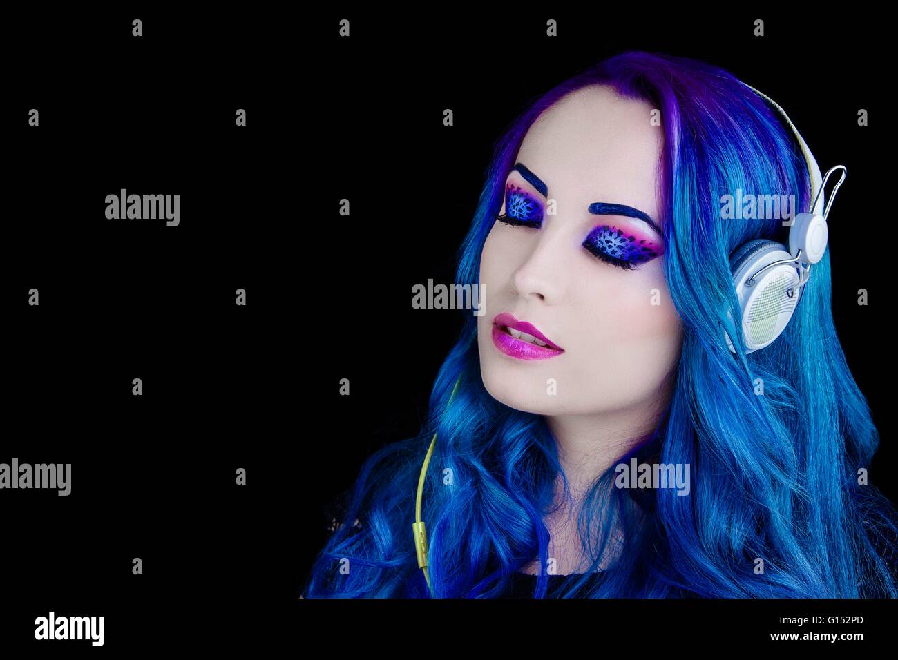 Portrait of a pretty girl with blue hair listening to music with eyes ...